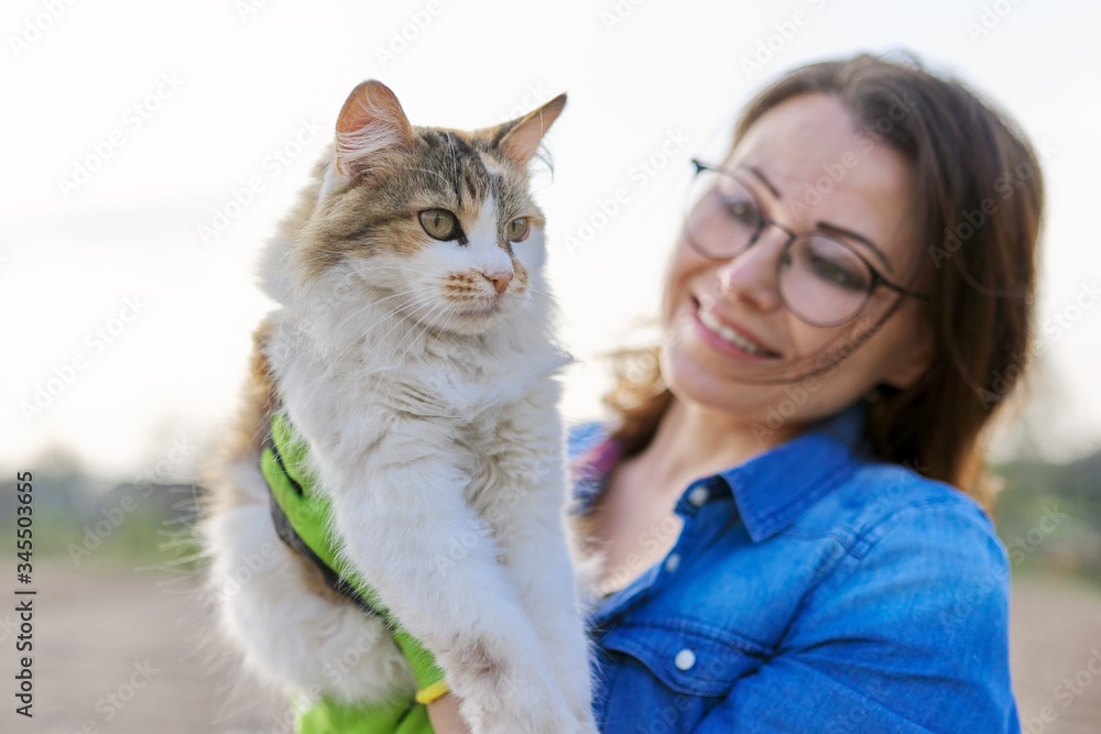 Outdoor woman holding domestic cat in arms and talking to her Outdoor woman holding domestic cat in arms and talking to her