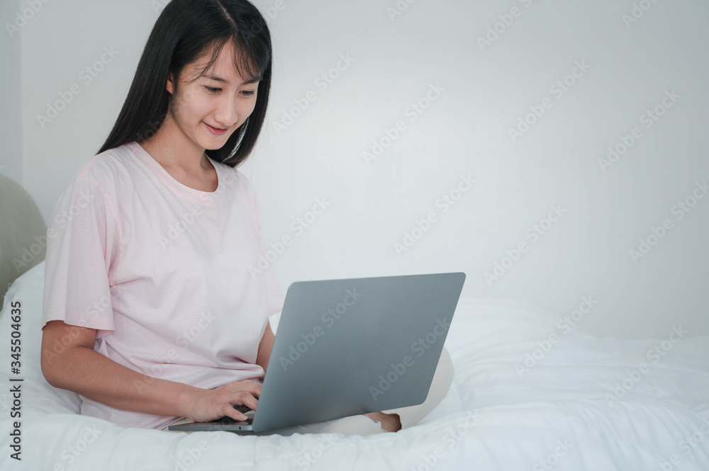 Happy casual beautiful asian woman working on a laptop sitting on the bed in the house. Happy casual beautiful asian woman working on a laptop sitting on the bed in the house.