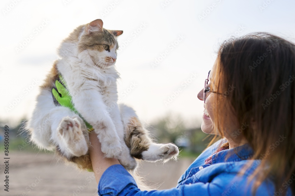 Outdoor woman holding domestic cat in arms and talking to her