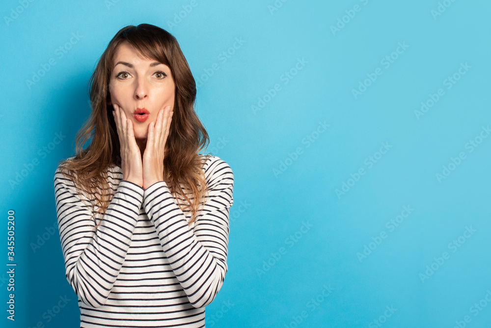 Portrait of a young friendly woman with a surprised face in a casual t-shirt on an isolated blue background. Emotional face. Gesture of surprise, delight, shock Portrait of a young friendly woman with a surprised face in a casual t-shirt on an isolated blue background. Emotional face. Gesture of surprise, delight, shock