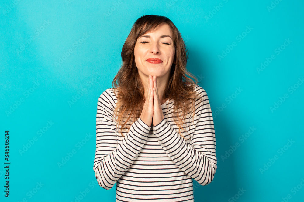 Young friendly woman with a smile in a casual t-shirt making prayer gesture with closed eyes on an isolated background. Emotional face. To ask for something from the universe or from God, make a wish Young friendly woman with a smile in a casual t-shirt making prayer gesture with closed eyes on an isolated background. Emotional face. To ask for something from the universe or from God, make a wish