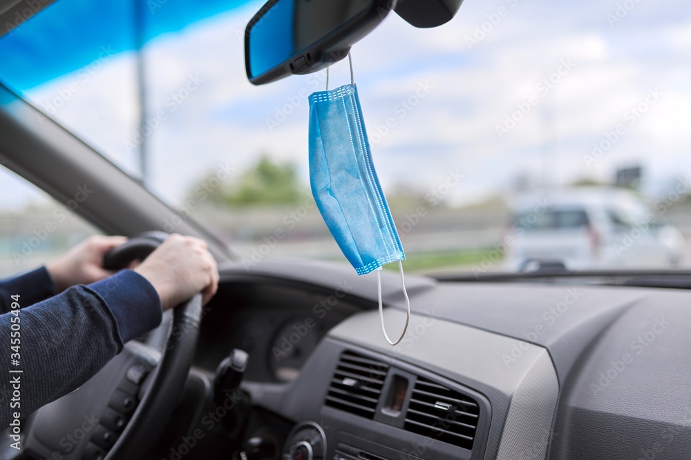 Protective medical mask of driver in car, mans hands on the steering wheel