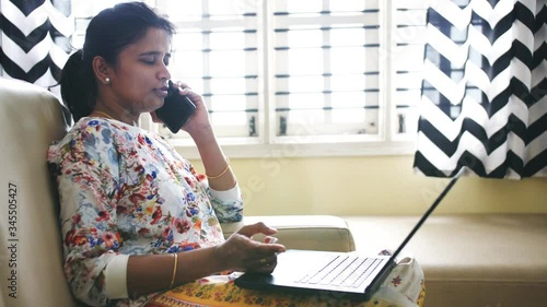 Closeup of an Indian business woman working from home sitting on a sofa and talking on phone