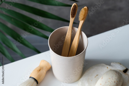 Eco friendly bamboo toothbrushes in glass with shaving brush and organic soap on table in bathroom. Zero waste, plastic free, sustainable lifestyle concept