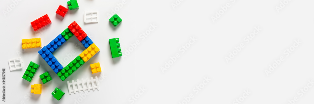 Unfinished house from the designer multi-colored details of the designer lie around on isolated white background. Educational toys, logic, new construction, new building. Banner. Flat lay, top view Unfinished house from the designer multi-colored details of the designer lie around on isolated white background. Educational toys, logic, new construction, new building. Banner. Flat lay, top view