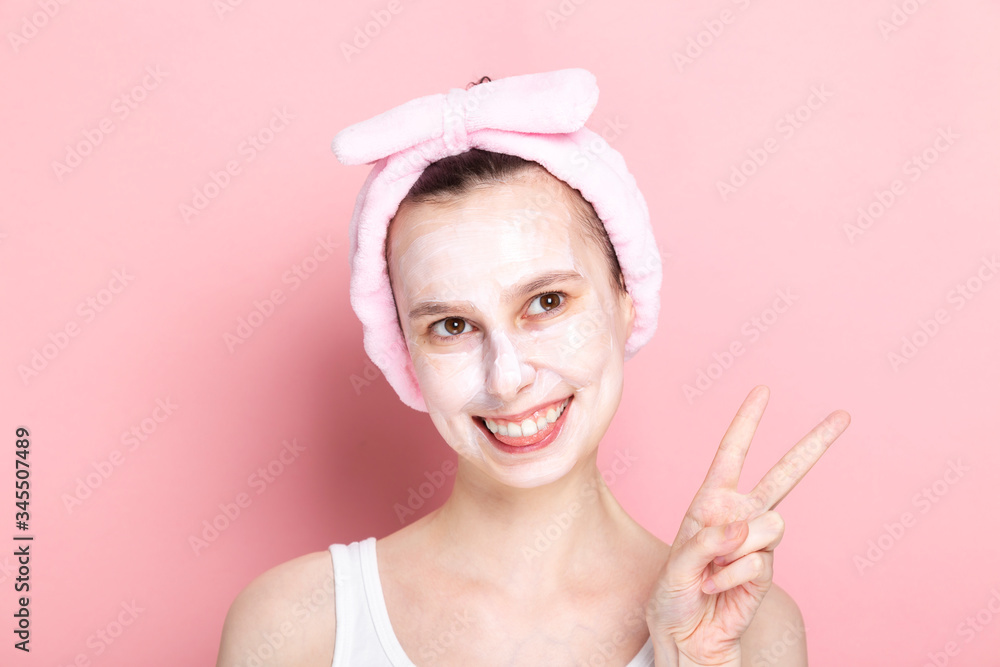Young girl with cosmetic mask on her face looks aside, smiles wide and shows fingers sign Young girl with cosmetic mask on her face looks aside, smiles wide and shows fingers sign