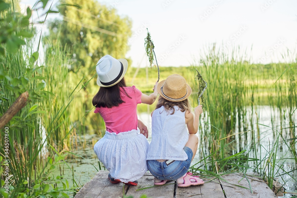 Girls children on wooden pier of lake in reeds, playing with water, talking