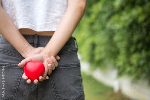 Selective focus of A woman with a heart shaped ball in her hand, hiding behind on blurred background and copy space