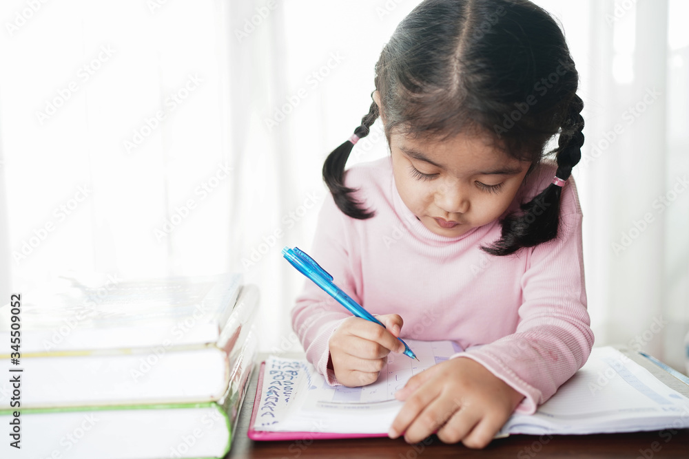 Asian student child girl writing on the paper book. Asian genius student doing a homework at home. education , study and learning concept. Asian student child girl writing on the paper book. Asian genius student doing a homework at home. education , study and learning concept.