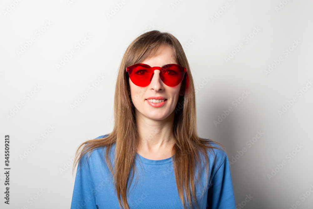 Portrait of a young friendly woman in casual blue t-shirt and red glasses smiling on isolated light background. Emotional face Portrait of a young friendly woman in casual blue t-shirt and red glasses smiling on isolated light background. Emotional face