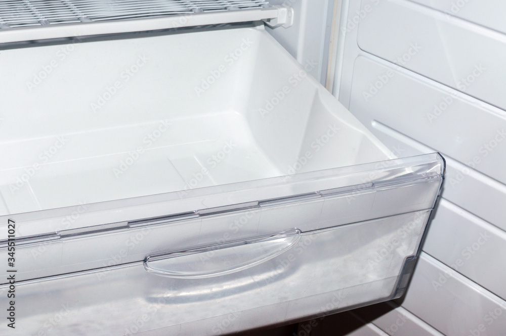 Open plastic white container drawer in refrigerator. Selective focus. Open plastic white container drawer in refrigerator. Selective focus.