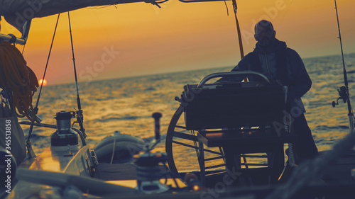 Sailor steering sailing boat with a rudder in dawn / twilight time on tje open sea. photo