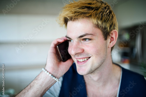 Close-up of young man with smartphone indoors at home, making phone call.