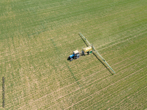Agricultural tractor sprays the crop field with chemicals. Aerial drone photo.