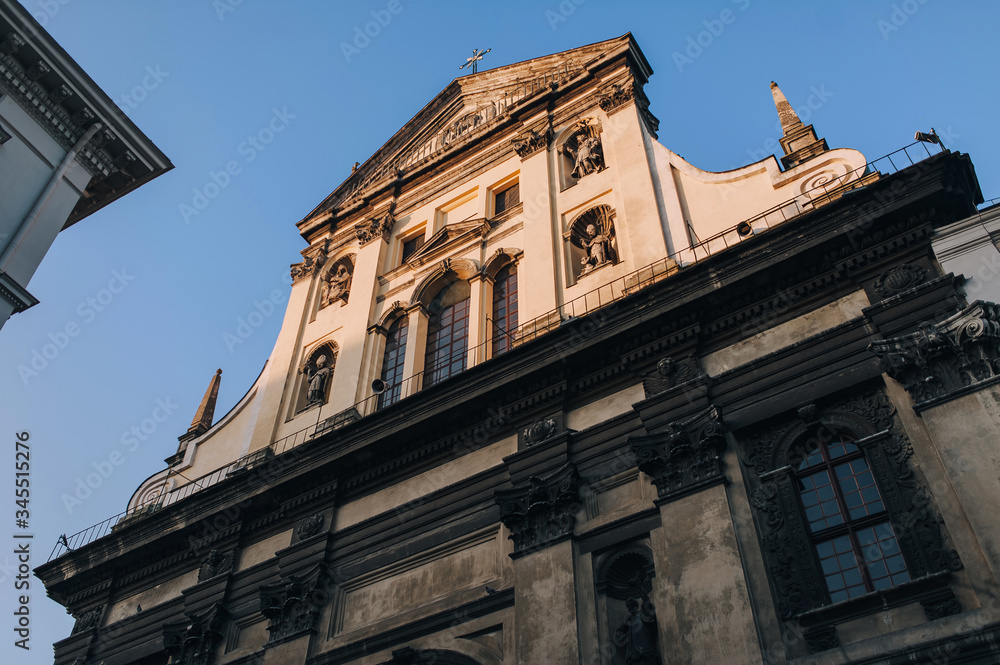 Antique baroque facade with window by decorative stucco on a beige wall with capitals and with sculptures of the Holy Fathers and the Blessed Virgin Mary in niches. Roof of Jesuit Church in Lviv.