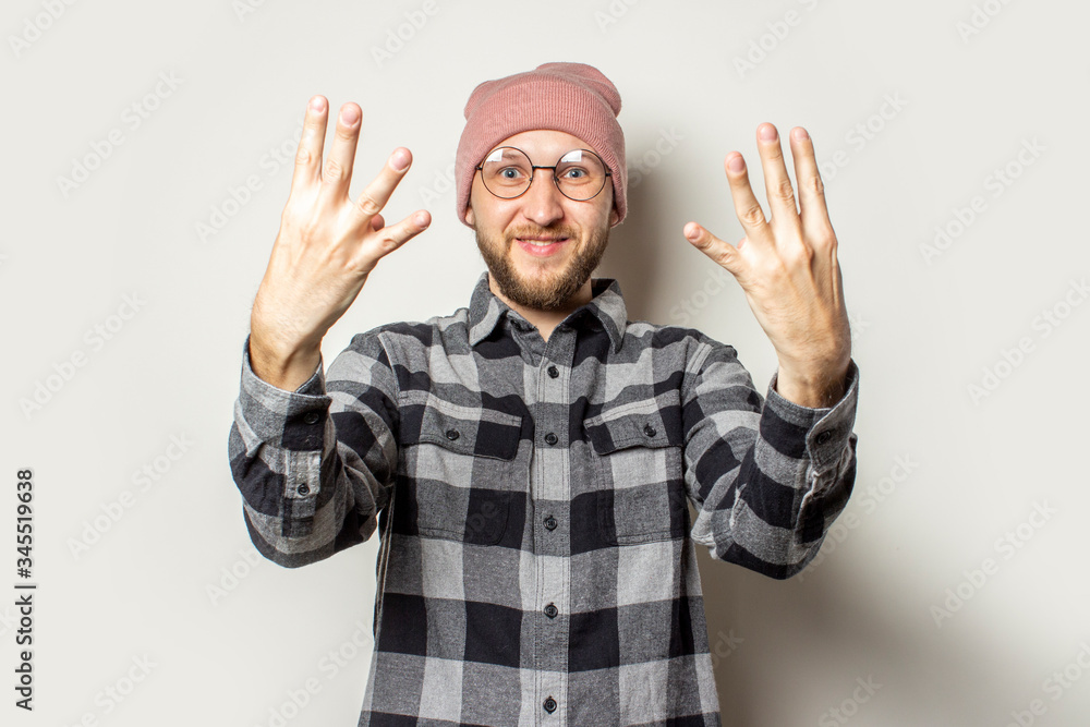 Portrait of a young man with a beard in a hat, a checkered shirt extended his arms in front of him with the back of his hand on an isolated light background. Emotional face. Stop gesture, enough Portrait of a young man with a beard in a hat, a checkered shirt extended his arms in front of him with the back of his hand on an isolated light background. Emotional face. Stop gesture, enough