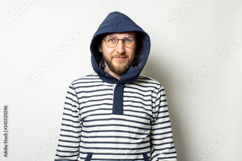 Portrait of a Bald Young man with a beard in glasses, a sweater with a hood on an isolated light background. Emotional face. Man in the hood