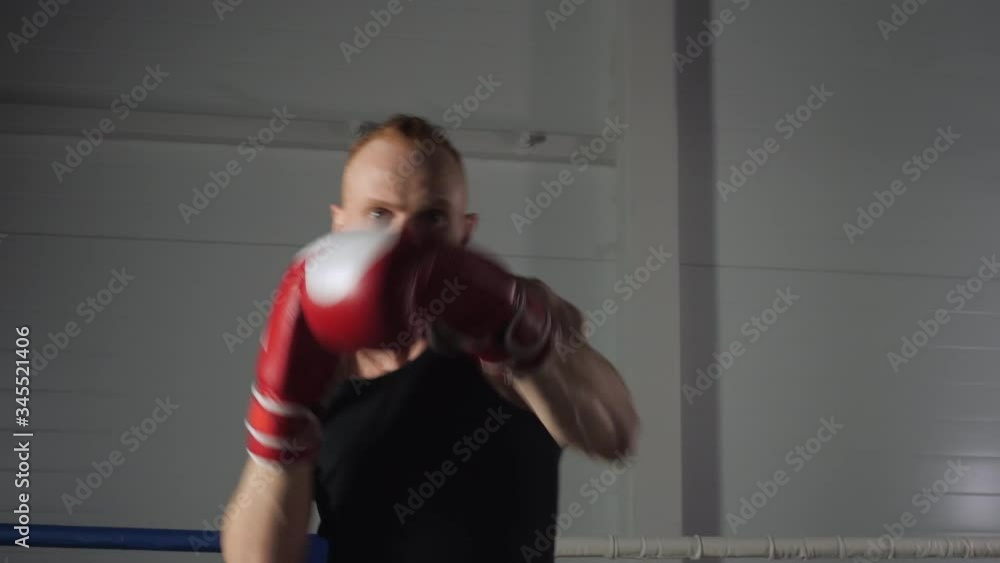 Fighter man in boxing gloves making strikes front camera. Boxer man boxing with shadow on fight ring. Kickboxer training punches in sport club Fighter man in boxing gloves making strikes front camera. Boxer man boxing with shadow on fight ring. Kickboxer training punches in sport club