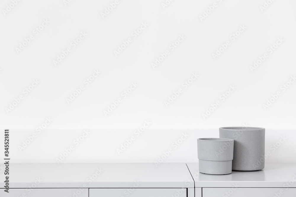 Empty grey cement flowerpots mockup on grey cabinet against a white wall. Empty grey cement flowerpots mockup on grey cabinet against a white wall.