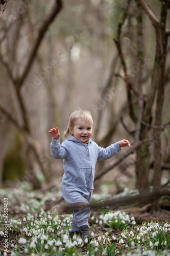 Little pretty girl in a clearing of snowdrops. A child walks in the spring forest.