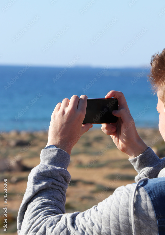 Young man take a picture of wonderful landscape before him. Teenager with his phone photographed monuments for subsequent memories from the travels.