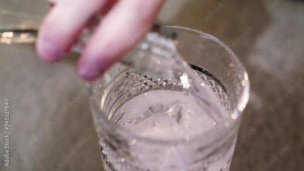 A person pouring sparkling water from a glass bottle to a transparent glass filled with cubes of ice A person pouring sparkling water from a glass bottle to a transparent glass filled with cubes of ice