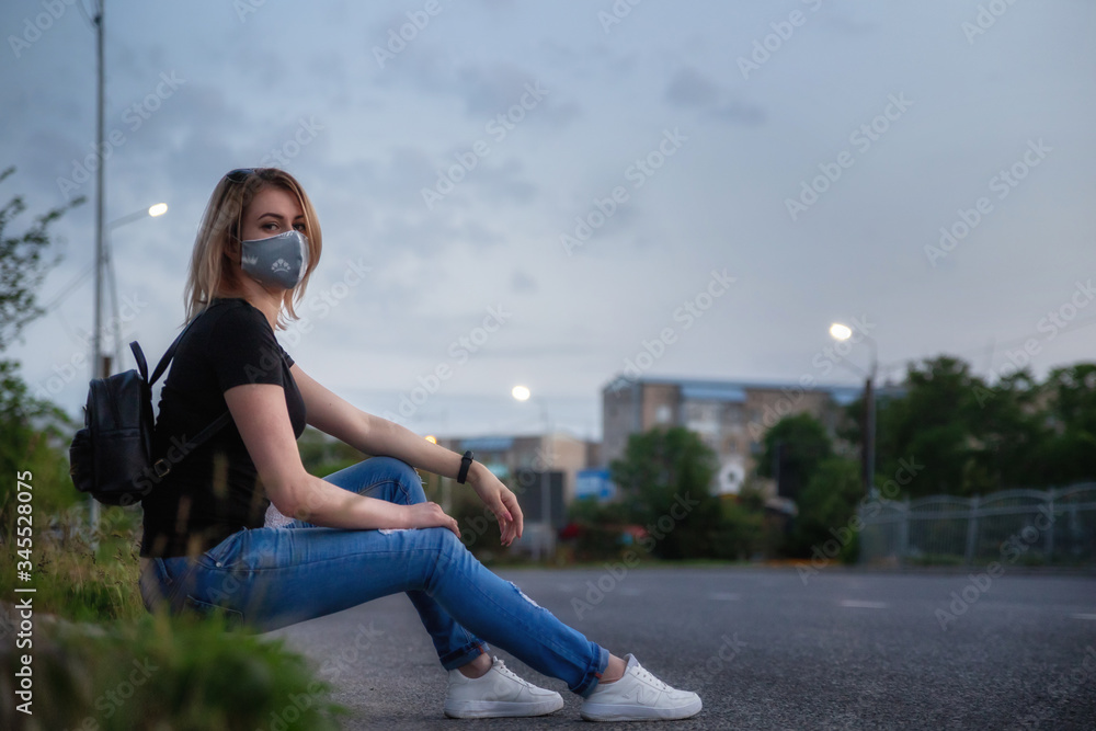 Fototapeta premium Girls in medical mask outdoors in an empty city. Sits on the side of the road. Health and prevention of viral epidemics, coronavirus, COVID-19, epidemic, infectious diseases, concept of quarantine