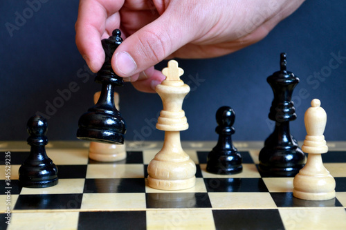 Male hand holding the black queen to defeat the white king on a chessboard on black background. Checkmate