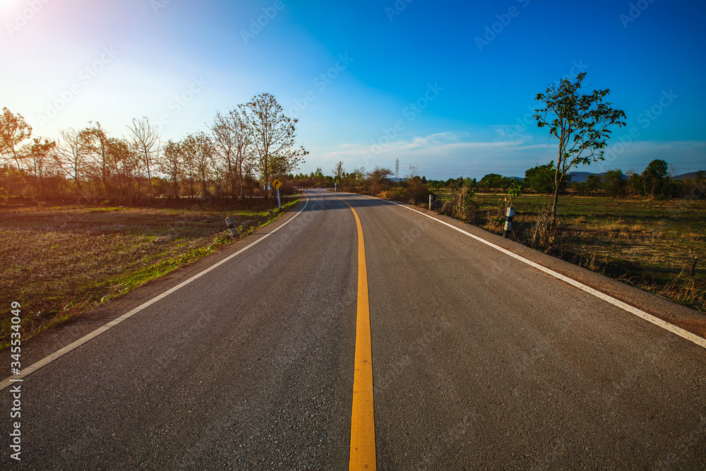 open road. Asphalt road through the green field and clouds on blue sky in summer day. 