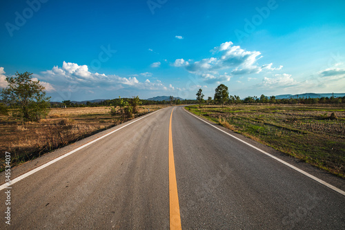 open road. Asphalt road through the green field and clouds on blue sky in summer day. 