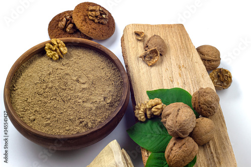 Walnut flour in ceramic bowl, walnuts with green leaves, cookies and firewood isolated on white background