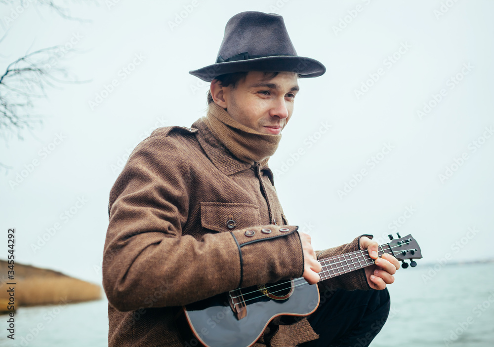 young man playing ukulele on stones at the lake young man playing ukulele on stones at the lake