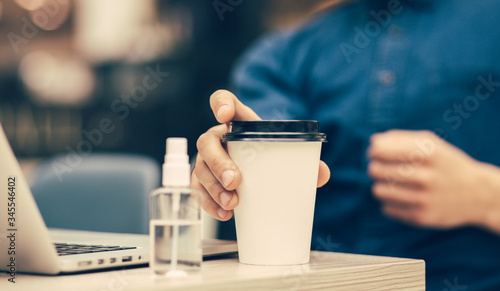 young man with a takeaway coffee sitting at a cafe table