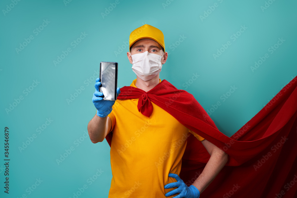 Courier dressed in superhero cloak and medical mask holds smartphone in his hand.