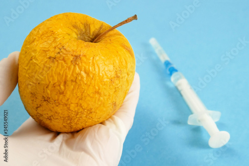 apple in genetic engineering laboratory with syringe and test tubes on blue background, gmo food concept