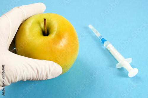 apple in genetic engineering laboratory with syringe and test tubes on blue background, gmo food concept