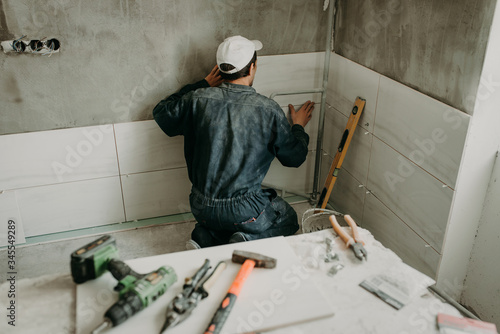 Worker repairman puts large ceramic tiles on the walls in the room photo