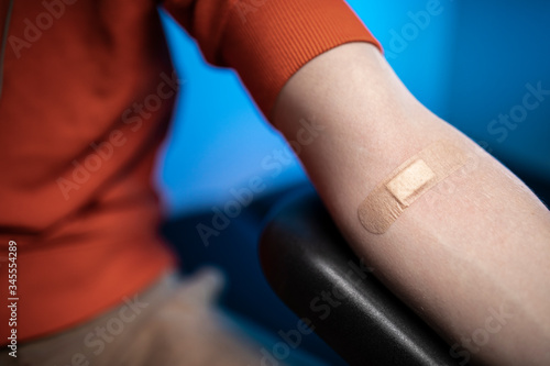 Praxis - An arm with a plaster of a young man with an orange sweatshirt after he was giving an injection. 