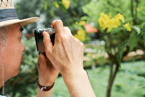 Close-up image of senior man taking photos of bloomig tree in his garden © DragonImages