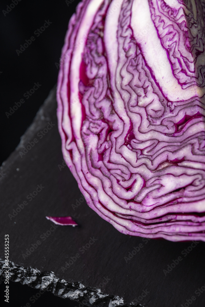 Obraz premium Close-up of open red cabbage, on black slate and black background, vertically