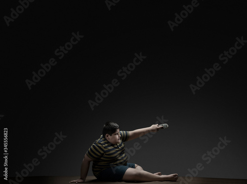 Young boy sitting on the floor and changing the channel with difficulty. (Obesity) 