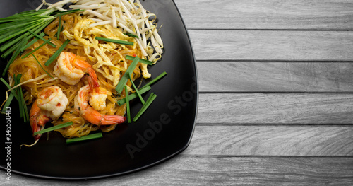 Stir fried noodles with prawns (Pud Thai) in black dish on wooden table photo