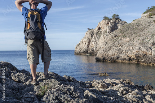 A young and bald man contemplating a seascape of on a beach without people in Mallorca. The man carries a backpack and it is early in the morning.