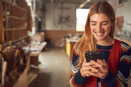 Foto Female Business Owner In Workshop Using Mobile Phone