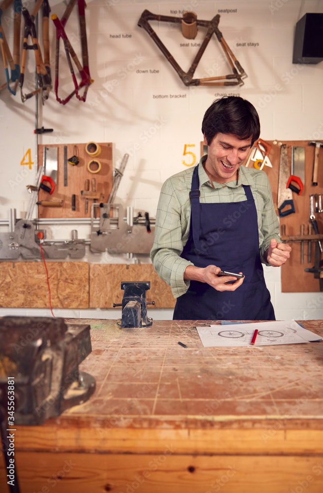 Excited Male Business Owner In Workshop Having Taken Call On Mobile Phone Excited Male Business Owner In Workshop Having Taken Call On Mobile Phone