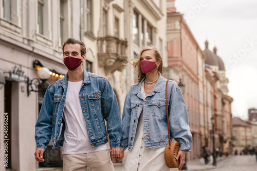 Couple wearing trendy fashionable protective masks, denim jackets, walking in empty street of European city during quarantine of coronavirus outbreak. Copy space for text