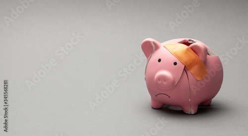 Broken piggy bank with band-aid on gray background