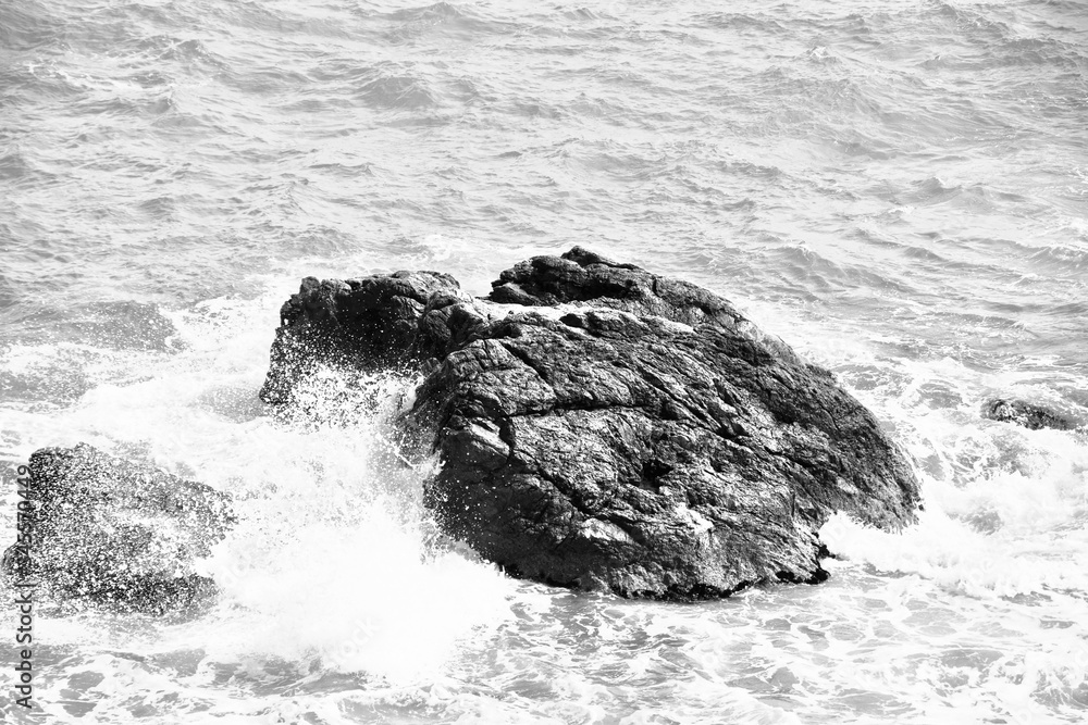 Les vagues de la mer déchaînée s'abattent sur de gros rochers. Photo en noir et blanc, haute résolution.