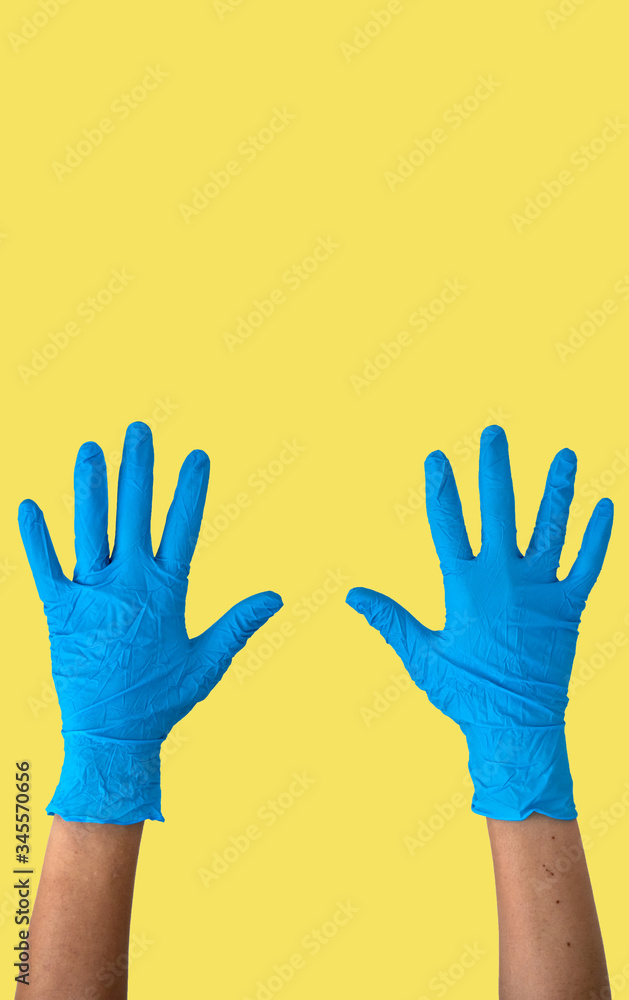 Obraz premium Human rising hands wearing blue disposable latex glove, rubber glove for professional medical safety and hygiene protection from Coronavirus disease COVID-19 and medical surgery on yellow background
