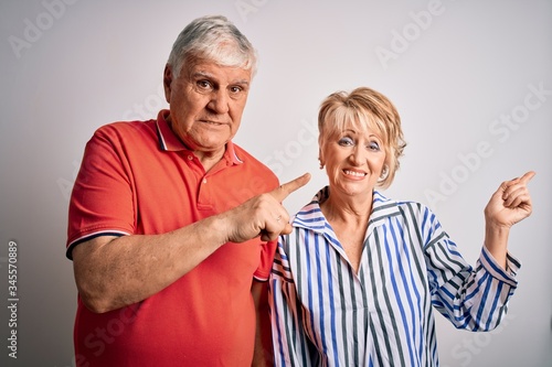 Senior beautiful couple standing together over isolated white background Pointing aside worried and nervous with both hands, concerned and surprised expression